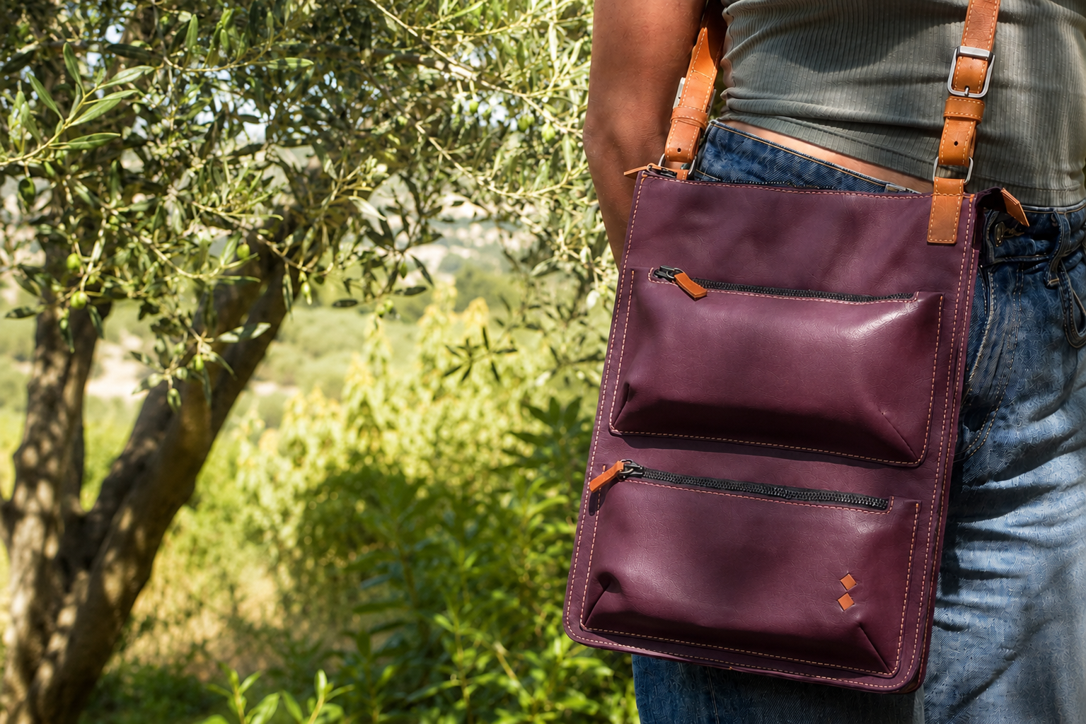 Person carrying a burgundy Karine leather bag outdoors with greenery in the background