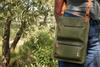 Person carrying the green crossbody Karine bag outdoors with trees in the background