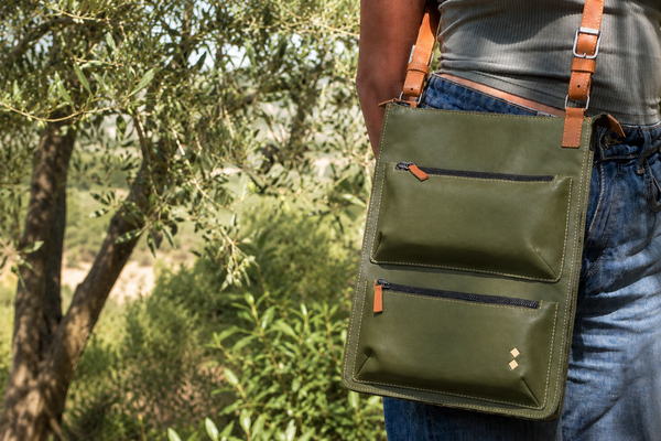 Person carrying the green crossbody Karine bag outdoors with trees in the background